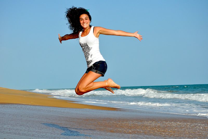 Freude am Strand Frau springt am Strand in die Luft mit glücklichem Gesichtsausdruck