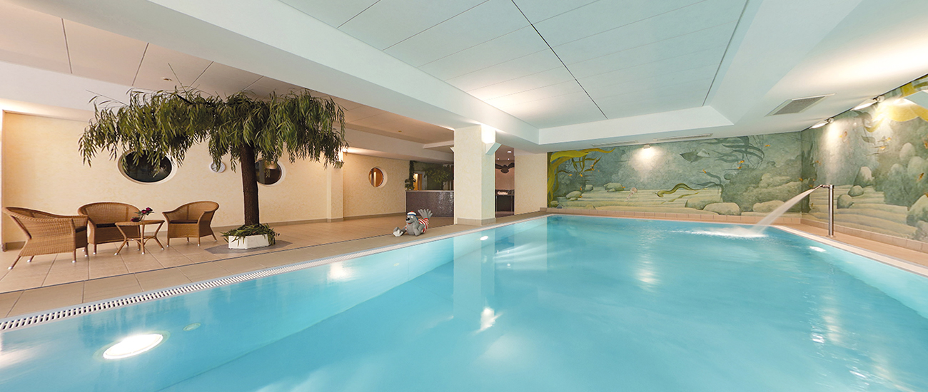 Entspannendes Schwimmbad mit Sitzgelegenheiten und dekorativen Elementen. Innenansicht eines hellen Schwimmbads mit Palmen, Sitzbereich und Wandmalereien.