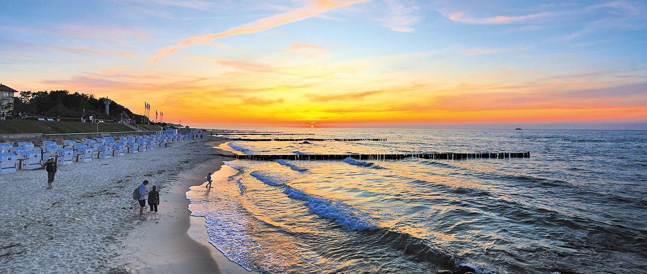 Sonnenuntergang am Strand mit Strandkörben und ruhigem Meer Strand mit Strandkörben und Personen im Sonnenuntergang, Wellen am Ufer