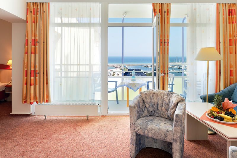 Hotelzimmer mit Balkon und Meerblick Hotelzimmer mit Meerblick, Balkon mit Tisch und Stühlen, Vorhänge, Sessel und Tisch mit Fruchtteller.
